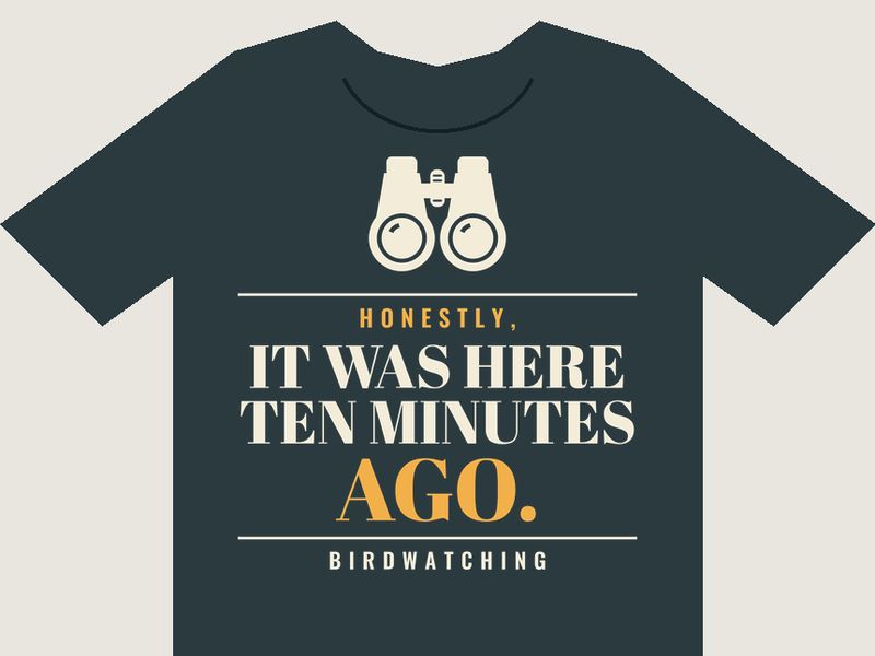 Charcoal T-shirt preview with cream binoculars above the words HONESTLY, IT WAS HERE TEN MINUTES AGO. in a field-guide serif, and BIRDWATCHING underneath.