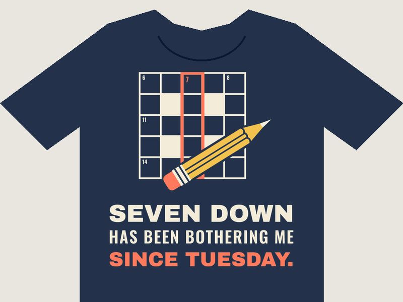 Navy T-shirt preview with a crossword grid, the 7 down column outlined in coral and a yellow pencil, above the words SEVEN DOWN HAS BEEN BOTHERING ME SINCE TUESDAY. in cream and coral.